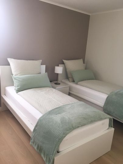 Een gezellig slaapkamer met twee eenpersoonsbedden. De muren zijn in zachte kleurnuances geschilderd, en er staat een kleine nachttafellamp.