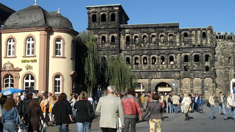 Une place animée avec beaucoup de monde et des bâtiments historiques. En arrière-plan se dresse une vieille façade en pierre.