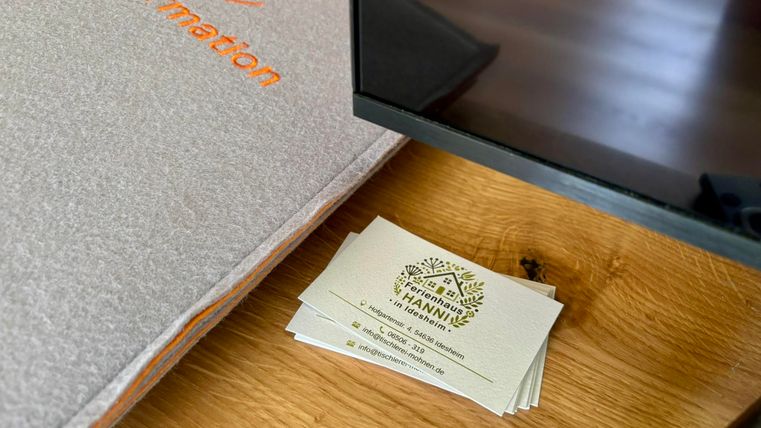 Ein Tisch mit einem informativen grauen Ordner und einer Handvoll Visitenkarten. Im Hintergrund ist ein Spiegel zu sehen.