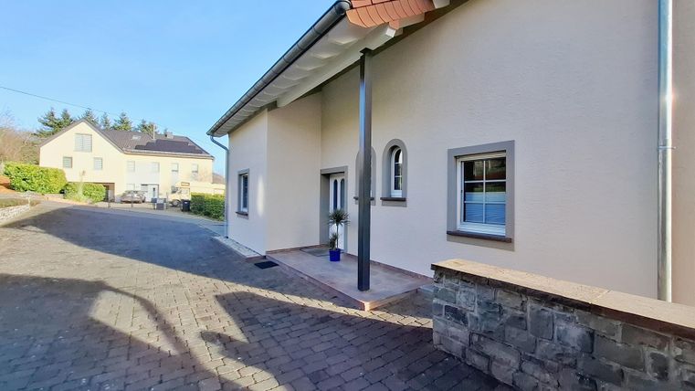 Ein modernes Haus mit einem gepflasterten Weg und klarer, blauer Himmel. Im Hintergrund sind weitere Gebäude sichtbar.