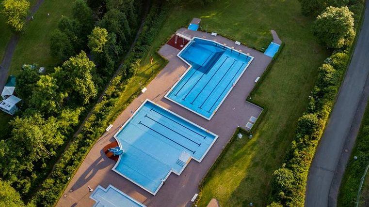Een uitgebreid zwembad met meerdere bassins, omringd door groene bomen. De blauwe wateroppervlakken stralen rust en ontspanning uit.