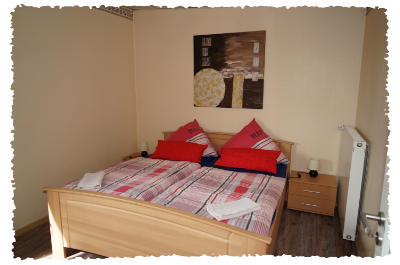 Une chambre confortable avec un grand lit et des coussins colorés. Sur le mur, une œuvre d'art moderne est accrochée, et les meubles sont en bois clair.