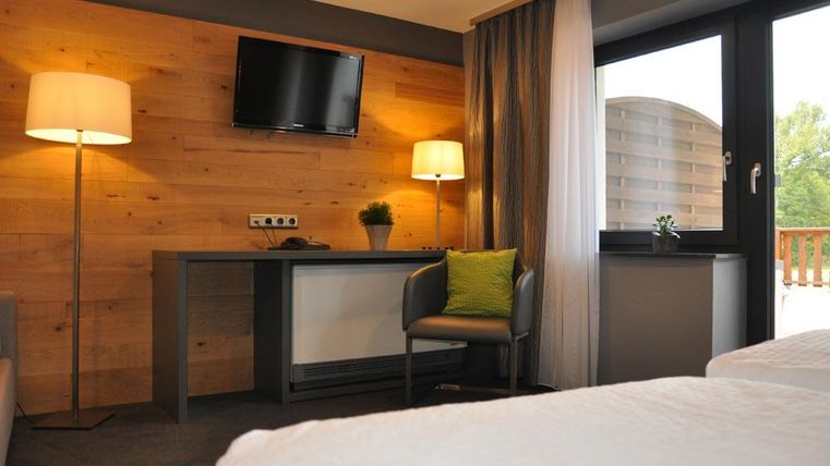 Une chambre d'hôtel moderne avec des murs en bois, un bureau et une télévision. Une lampe lumineuse et un coussin vert donnent une atmosphère accueillante à la pièce.
