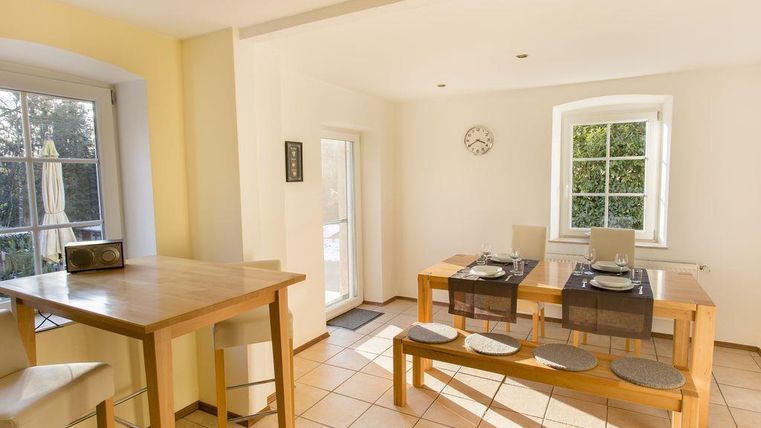 A bright and modern kitchen with a dining area. The table is set and there is a large window door that leads outside.
