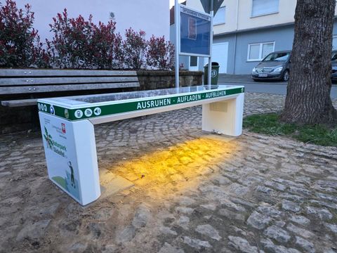 Ein kreatives Baumhaus mit Holzstapel und einem kleinen Eingang. Es steht in einer grünen Wiese, umgeben von einem Holzzaun.