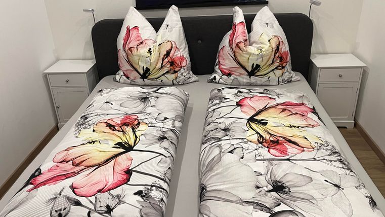 Une chambre confortable avec un lit double et des couvertures colorées à motif floral. À côté du lit, il y a deux tables de nuit.