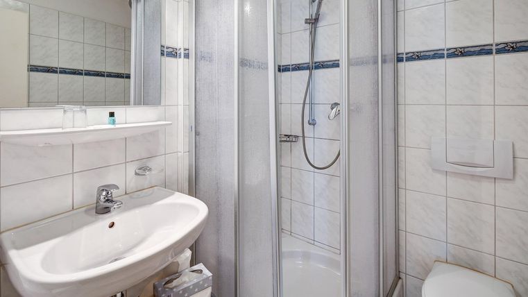 Une salle de bain moderne avec une douche, un lavabo et des toilettes. Les murs sont recouverts de carreaux blancs.