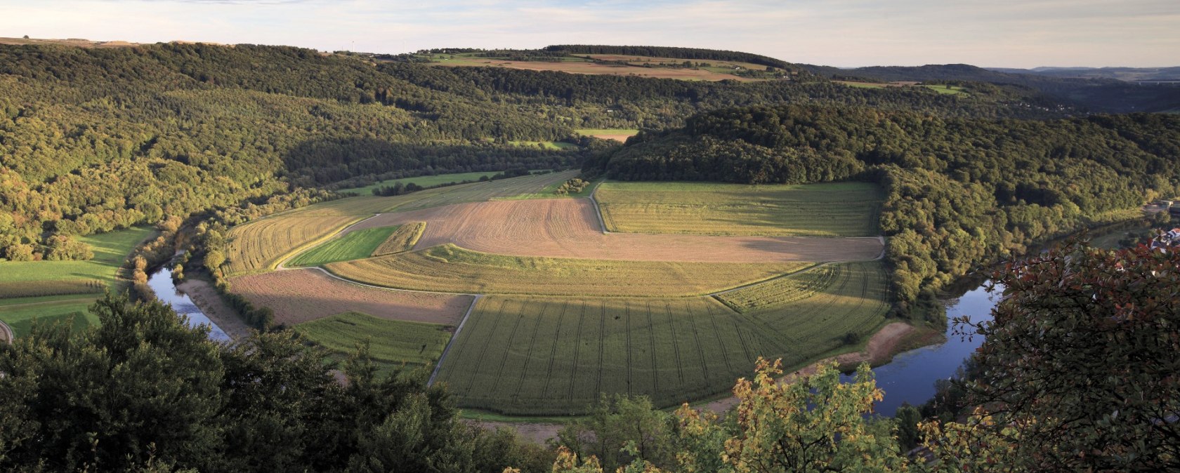Panoramablick auf eine Flusslandschaft mit Feldern und Wäldern im Sonnenuntergang. Der Fluss schlängelt sich durch die grüne Landschaft., © Naturpark Südeifel, C. Schleder