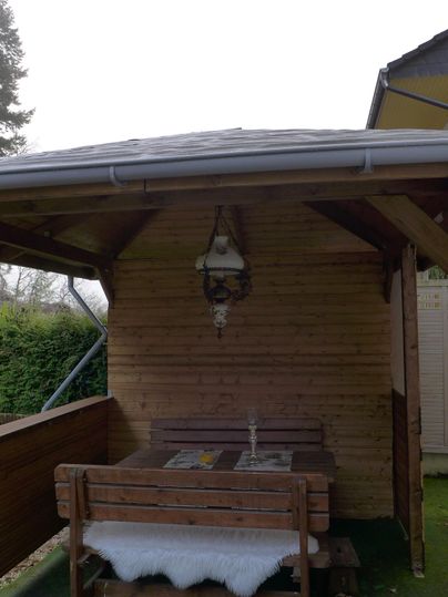 Eine gemütliche Holzterrasse mit einem Tisch und einer Bank. Der Bereich ist überdacht und bietet eine ruhige Atmosphäre.