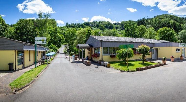 Een schilderachtige locatie met gele gebouwen omgeven door groene natuur. De heldere lucht en de bomen geven de omgeving een uitnodigende sfeer.