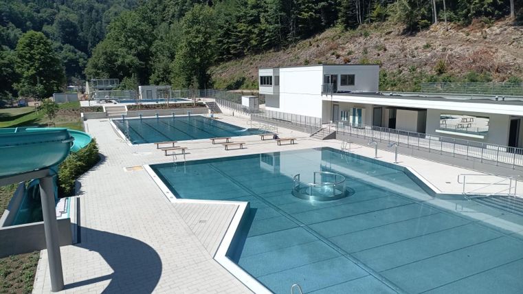 A modern swimming pool with several basins and clear blue water. The facility is surrounded by trees and has plenty of space to relax.