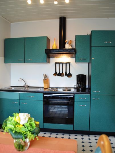 A modern kitchen with green cabinets and a black stove. A blooming vase is on the table.