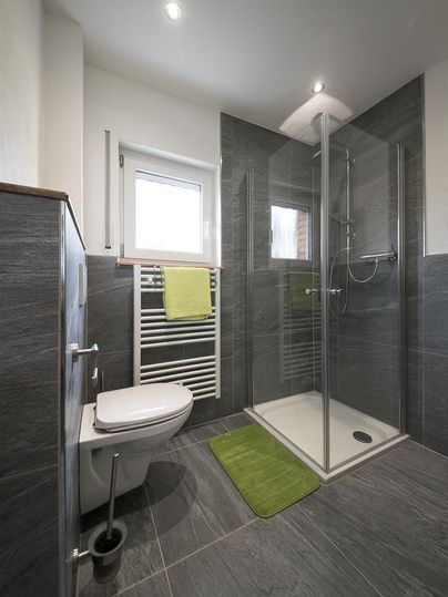 Une salle de bain moderne avec une douche et des toilettes. La pièce a des tuiles grises et est bien éclairée.