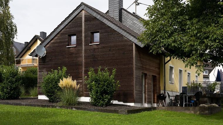 Une maison moderne avec une façade en bois et un jardin bien entretenu. À côté se trouve un autre bâtiment de couleurs claires.