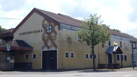 Ein gemeindliches Gebäude mit der Aufschrift „Gemeindehaus“. Es ist von Bäumen umgeben und hat einen funktionalen Baustil.