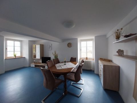 Ein heller Raum mit einem runden Tisch und Stühlen. Große Fenster bringen Tageslicht in den Raum.