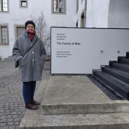 Une personne se tient devant un bâtiment avec un panneau qui indique "The Family of Man". L'endroit a l'air moderne et accueillant.