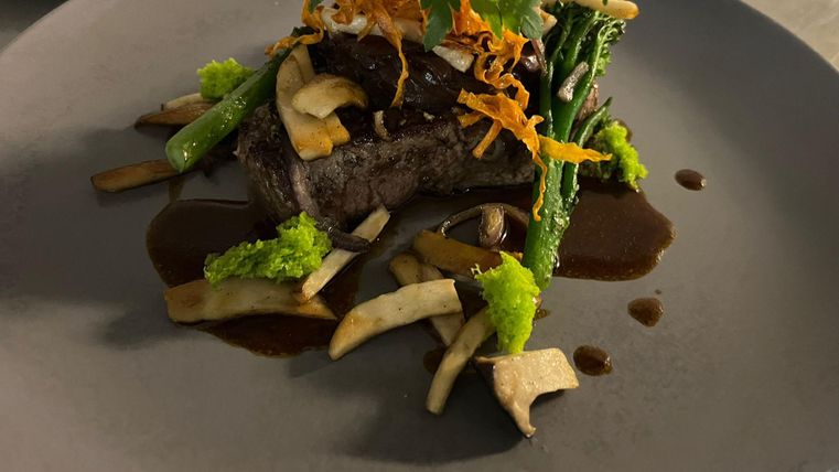 Un plat savamment présenté avec de la viande tendre, des légumes verts et une sauce riche. La décoration se compose d'herbes fraîches et de légumes croquants.