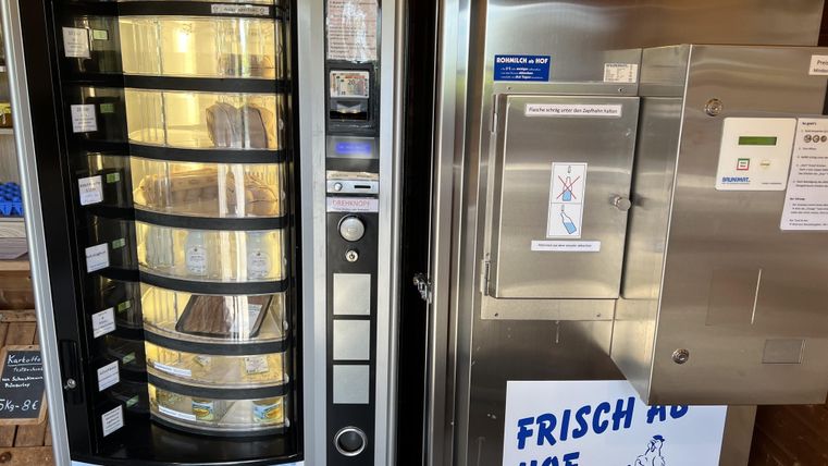 A vending machine with snacks and drinks stands next to a refrigerator that offers fresh products. On the refrigerator, there is a sign that says "FRESH FROM THE FARM."