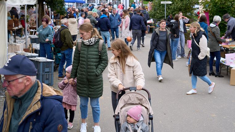 Eine belebte Marktstraße mit vielen Menschen und Verkaufsständen. Familien schlendern entlang der Stände und genießen die Atmosphäre.