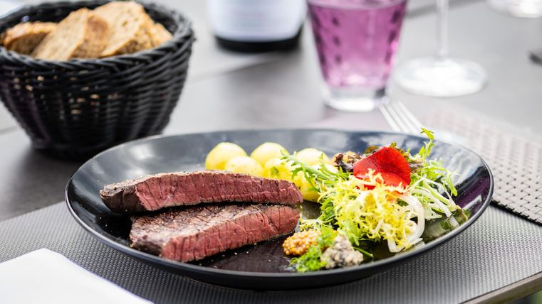 Une belle assiette avec un steak juteux, des accompagnements de pommes de terre et une salade fraîche. En arrière-plan, on peut voir du pain et une boisson.