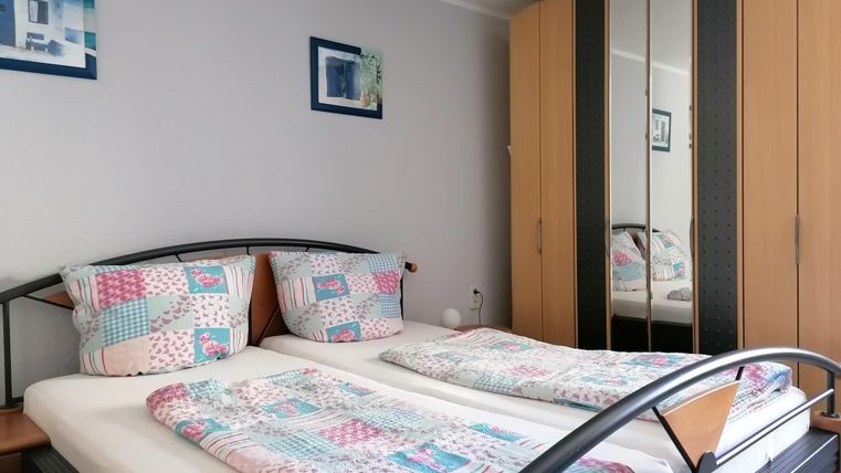 Ein gemütliches Schlafzimmer mit einem Doppelbett und bunten Bettdecken. An der Wand hängen Bilder, und ein großer Spiegelschrank steht daneben.