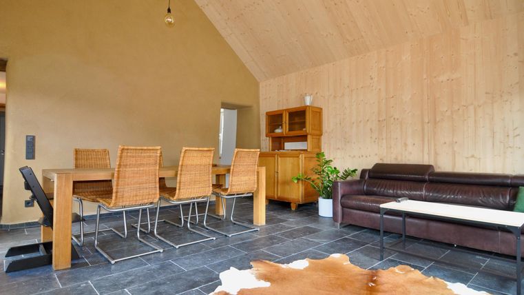 Ein stilvolles Wohnzimmer mit Holzwänden und einem gemütlichen Esstisch aus Holz. Neben dem Tisch steht eine moderne Couch und ein Teppich aus Tierfell.