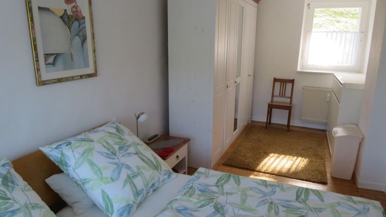 Een heldere slaapkamer met een tweepersoonsbed en frisse beddengoed. Er is een kast, een stoel en veel daglicht.