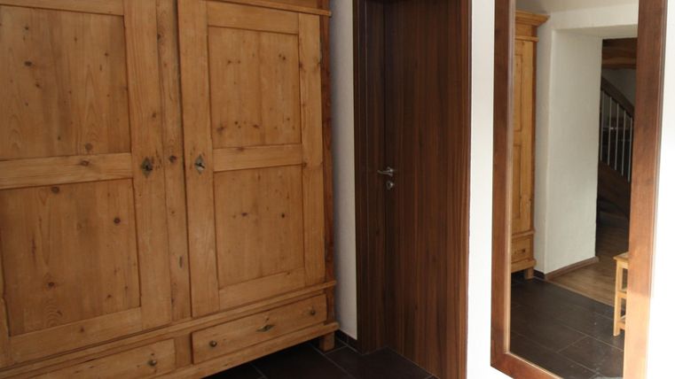 Ein gemütlicher Flur mit einem großen Holzschrank und einem Spiegel. Die Wände sind hell und der Boden ist dunkel gefliest.