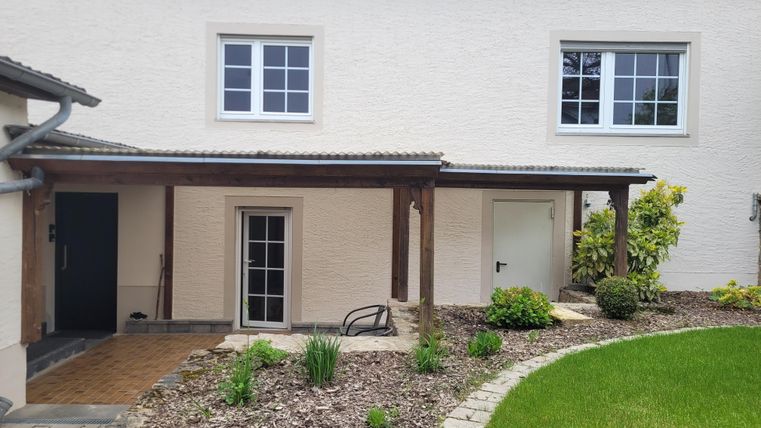 Ein modernes Haus mit einer gepflegten Grünfläche. Der Eingangsbereich ist von Pflanzen und einem Holzveranda umgeben.