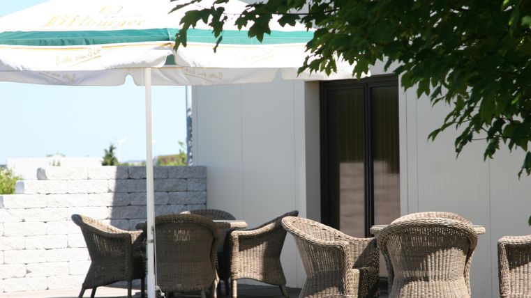 Een gezellige buitenruimte met een luifel en een tafel. Rondom de tafel staan meerdere gevlochten stoelen.