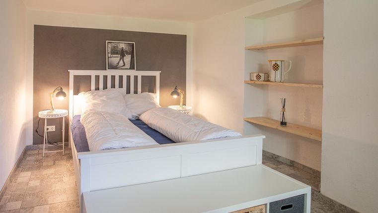 Ein stilvolles Schlafzimmer mit einem weißen Bett und sanfter Beleuchtung. Regale bieten zusätzlichen Stauraum und das Gesamtbild ist modern und einladend.