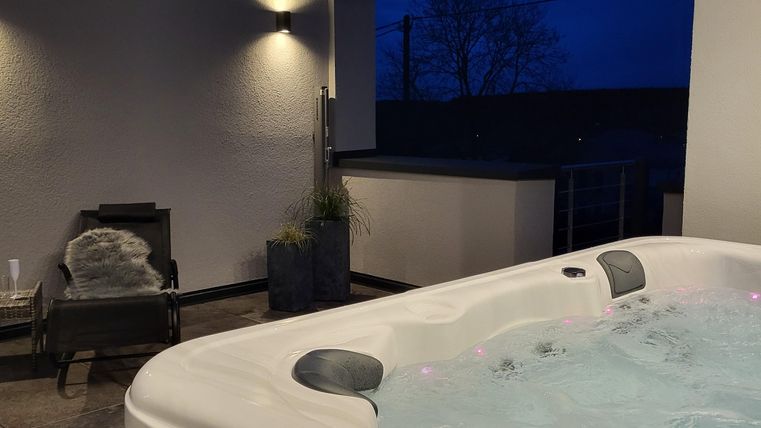 Un jacuzzi sur une terrasse moderne la nuit. Une douce lumière et une atmosphère détendue créent un environnement accueillant.