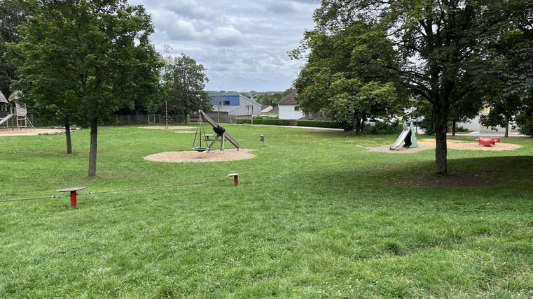 A spacious playground with grassy areas and various play equipment. In the background, some trees and buildings can be seen.