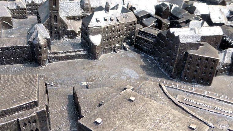 Eine detaillierte 3D-Miniaturansicht einer Stadt mit Gebäuden und Straßen. Die Modelle sind in Bronze gefertigt und zeigen eine historische Architektur.