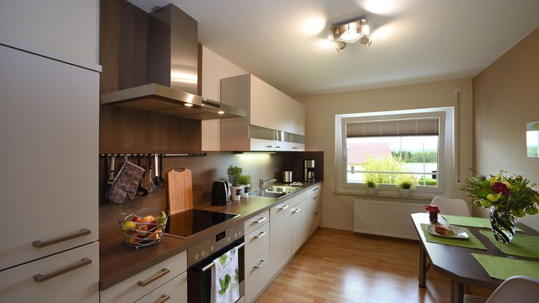 Une cuisine moderne avec des meubles en bois et blancs. Il y a une atmosphère lumineuse et beaucoup d'espace pour la préparation des repas.