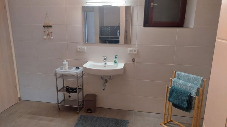 A modern bathroom with a sink and a large mirror. There is a towel holder and a small shelf for toiletries.