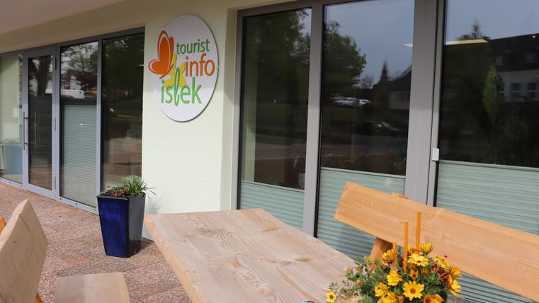 Un centre d'information moderne avec de grandes fenêtres. Dehors, il y a une table en bois avec des fleurs colorées dans un pot.