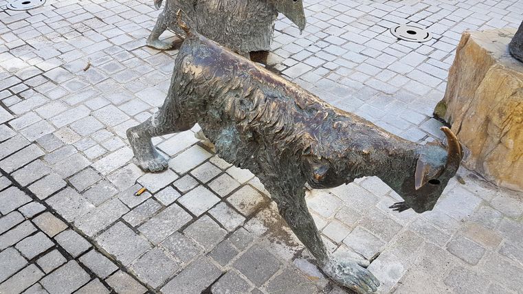 Eine Gruppe von Tierstatuen, die Ziegen darstellen, steht auf einem gepflasterten Platz. Die Statuen sind aus Bronze und zeigen detaillierte Texturen.