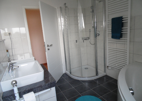 Een moderne badkamer met een douche en een bad. De muren zijn betegeld en de inrichting is eenvoudig en elegant.