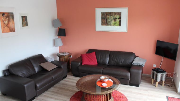 Ein gemütliches Wohnzimmer mit zwei sofas in Braun und einem runden Couchtisch. Die Wände sind teilweise orange gestrichen und einige Bilder hängen dekorativ an der Wand.