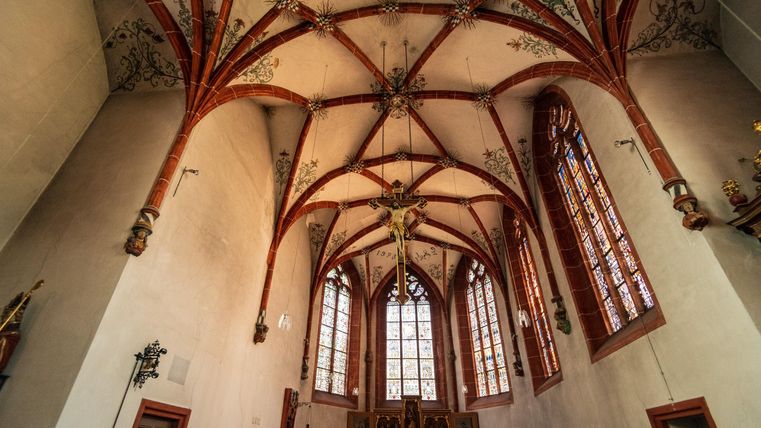 Eine beeindruckende Kirchenkuppel mit roten Gewölben und kunstvollen Verzierungen. Große Fenster lassen viel Licht herein, was eine helle Atmosphäre schafft.