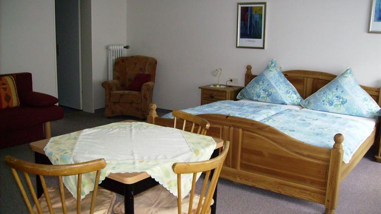 Ein gemütliches Zimmer mit einem Doppelbett und einem roten Sofa. Der Raum enthält einen Tisch mit Stühlen und eine angenehme Atmosphäre.