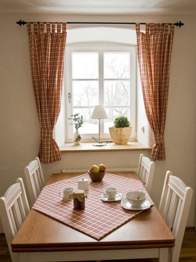 Een gezellige eetruimte met een houten tafel, witte stoelen en een geruit tafelkleed. Het raam laat veel daglicht binnen en biedt een rustige sfeer.