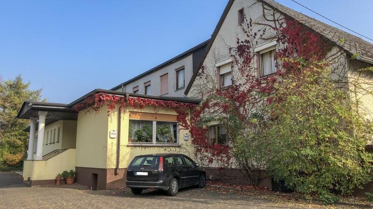 Un bâtiment avec une façade jaune, partiellement recouvert de plantes. Devant la maison se trouve une voiture noire.