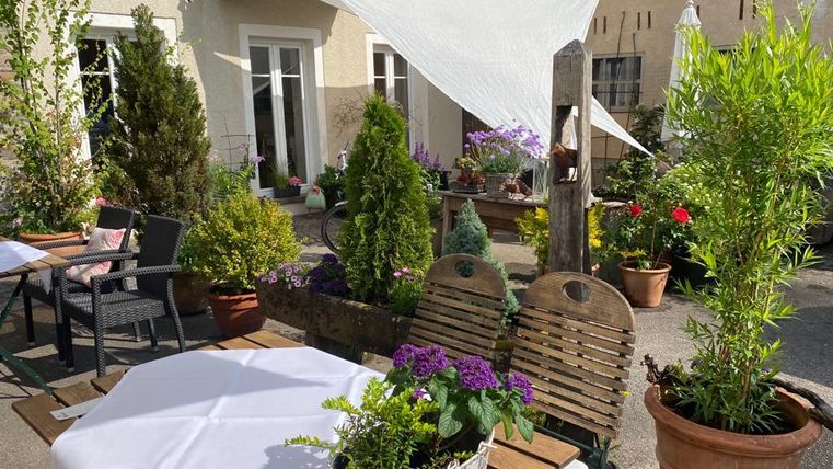 Un patio confortable avec des plantes fleuries et des tables. La protection solaire et les espaces verts créent une atmosphère accueillante.