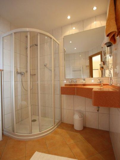 Ein modernes Badezimmer mit einer Runddusche und einem Waschbecken. Die Wände sind hell gefliest und das Licht ist angenehm.