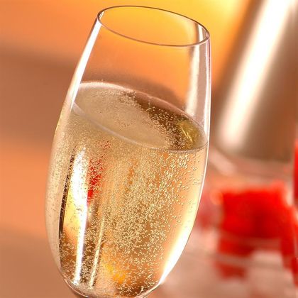 Een glas met bruisende drank staat voor een vage achtergrond. Het is elegант en uitnodigend, ideaal voor feestelijke gelegenheden.