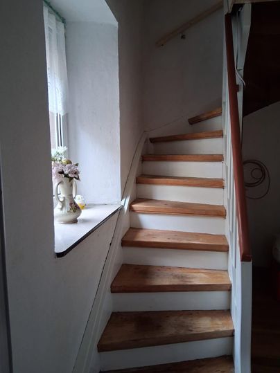 Un large escalier avec des marches en bois. Une fenêtre ornée de fleurs embellit le mur.