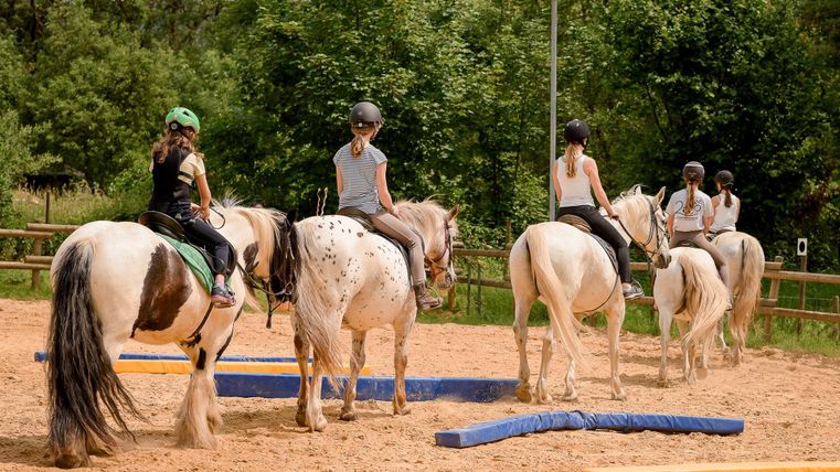 Ruiters op paarden in het zandgebied voor de training. Ze oefenen op verschillende hindernissen onder een heldere lucht.
